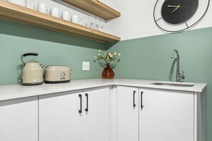 A kitchen with white cabinets, a kettle, a toaster, a vase with flowers, a sink, and a clock on the wall.