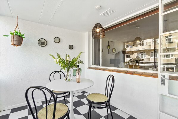 A dining area with a white table, black and white checkered floor, black metal chairs, and a hanging plant.