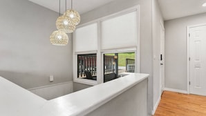 Un interior moderno con un mostrador blanco, una ventana con persianas y una lámpara colgante.