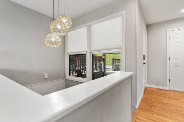 A modern interior with a white counter, a window with blinds, and a hanging light fixture.