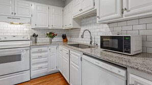 Una cocina con armarios blancos, encimera de granito, pileta de acero inoxidable, microondas y lavavajillas.