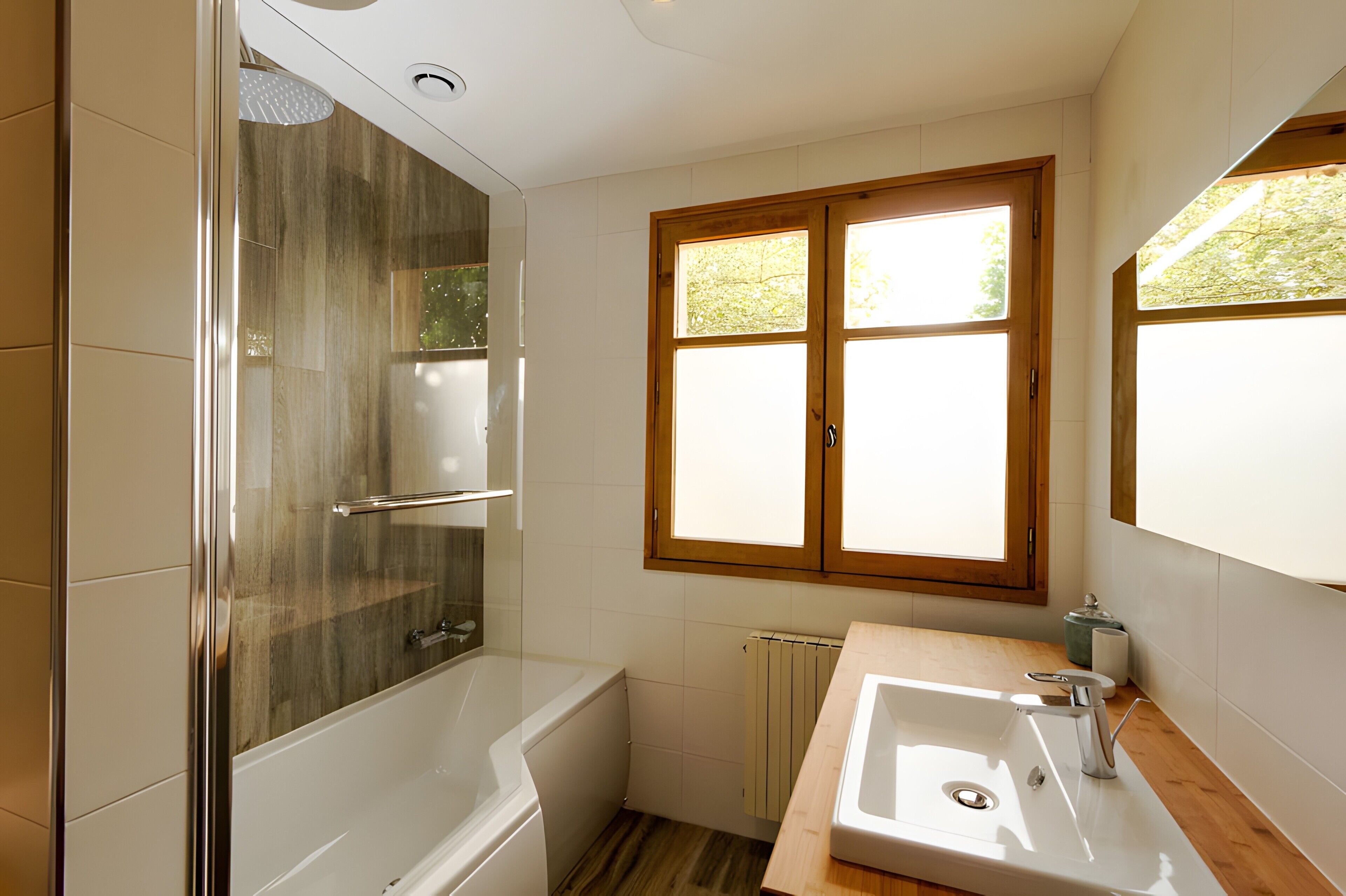 A bathroom with a glass-enclosed shower, a bathtub, a sink with a mirror, and a window with a view of greenery.