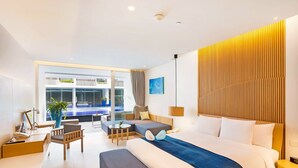 A modern hotel room with a large bed, a desk, a chair, a small table, and a view of a pool and outdoor area. - Ace of Hua Hin Resort - Ace Deluxe Pool Access (Cha-am)