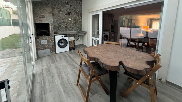 A modern kitchen with a stone backsplash, built-in appliances, and a dining area with a wooden table and chairs. - Spacious villa with garden and barbecue, near Serra de Sintra, beach and Cascais (Alcabideche)