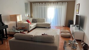 A living room with a sofa, a glass coffee table, a lamp, a television, and a piano. - Spacious villa with garden and barbecue, near Serra de Sintra, beach and Cascais (Alcabideche)