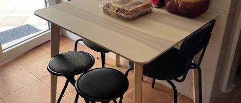Una cocina con una mesa, sillas, un tostador, una cesta con productos y una ventana.