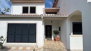 A two-story house with a tiled roof, a large garage door, and a small porch area with a potted plant. - Spacious villa with garden and barbecue, near Serra de Sintra, beach and Cascais (Alcabideche)