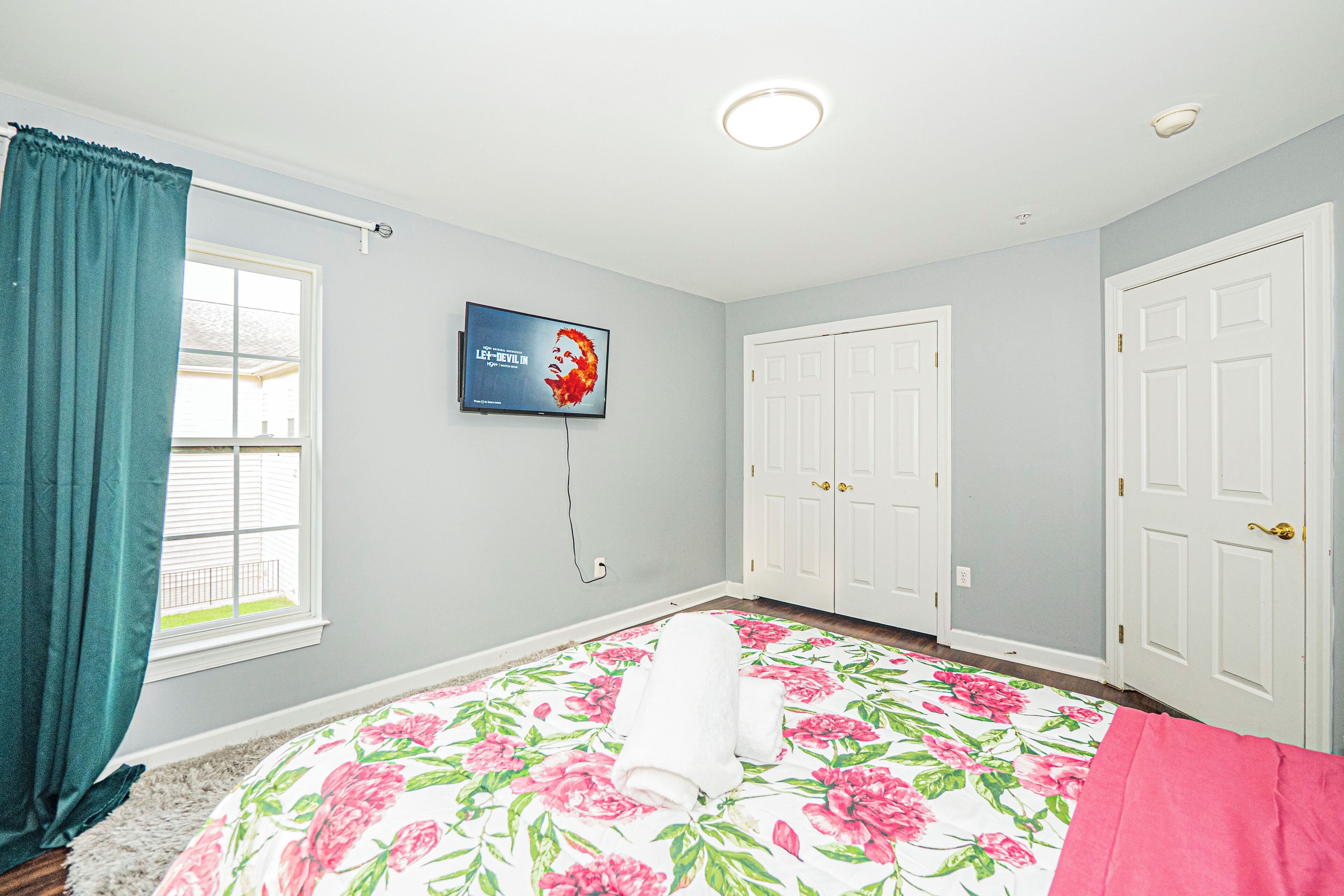 A bedroom with a floral bedspread, a television mounted on the wall, and two white doors.