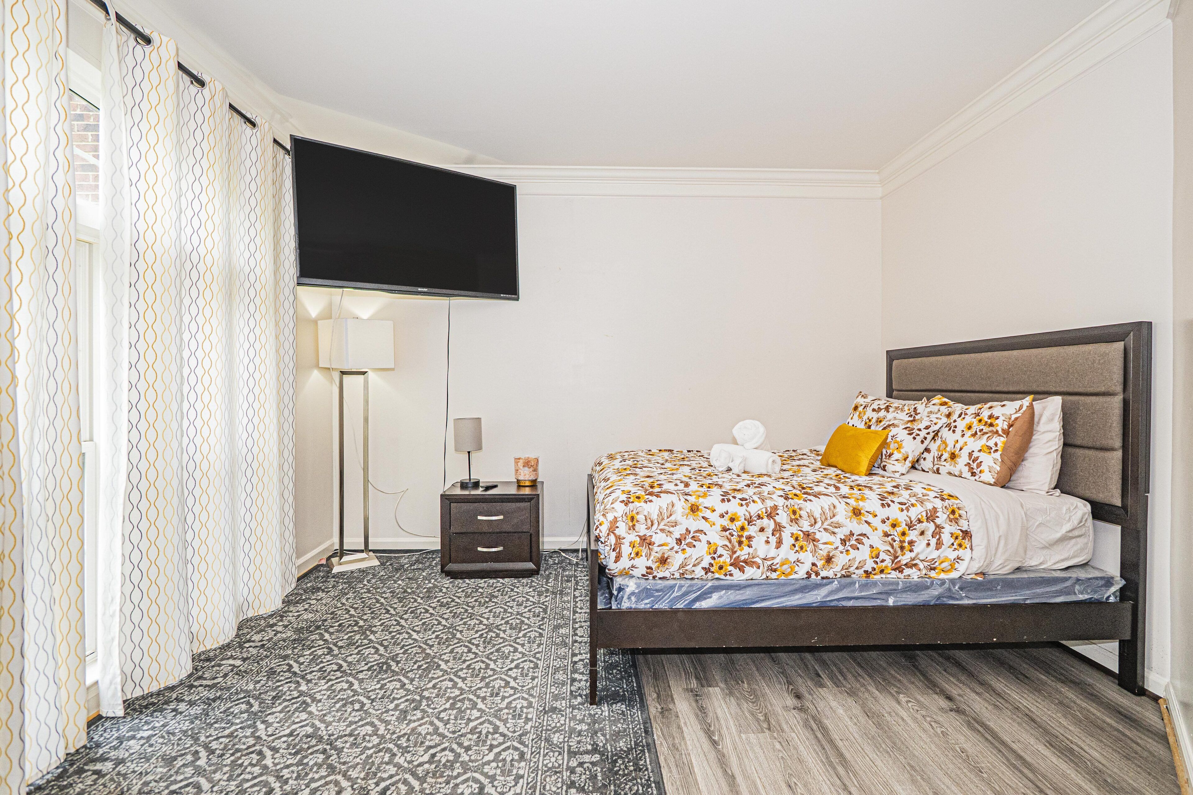 A bedroom with a bed, a TV, a nightstand, and a patterned rug.