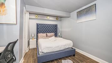 Ein Schlafzimmer mit einer gepolsterten Kopfteile, einem Bett mit weißer Bettwäsche, einem kleinen Nachttisch mit Lampe und einem gerahmten Bild an der Wand.