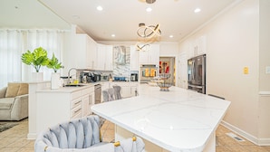 A modern kitchen with white cabinetry, a large island, and a stainless steel refrigerator.
