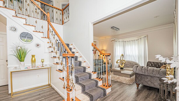 A staircase with a white and gold design, a living room with a grey sofa, and a decorative console table.