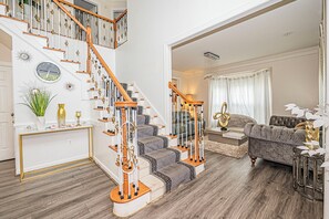 Un escalier aux motifs blancs et dorés, un salon avec un canapé gris et une console décorative.