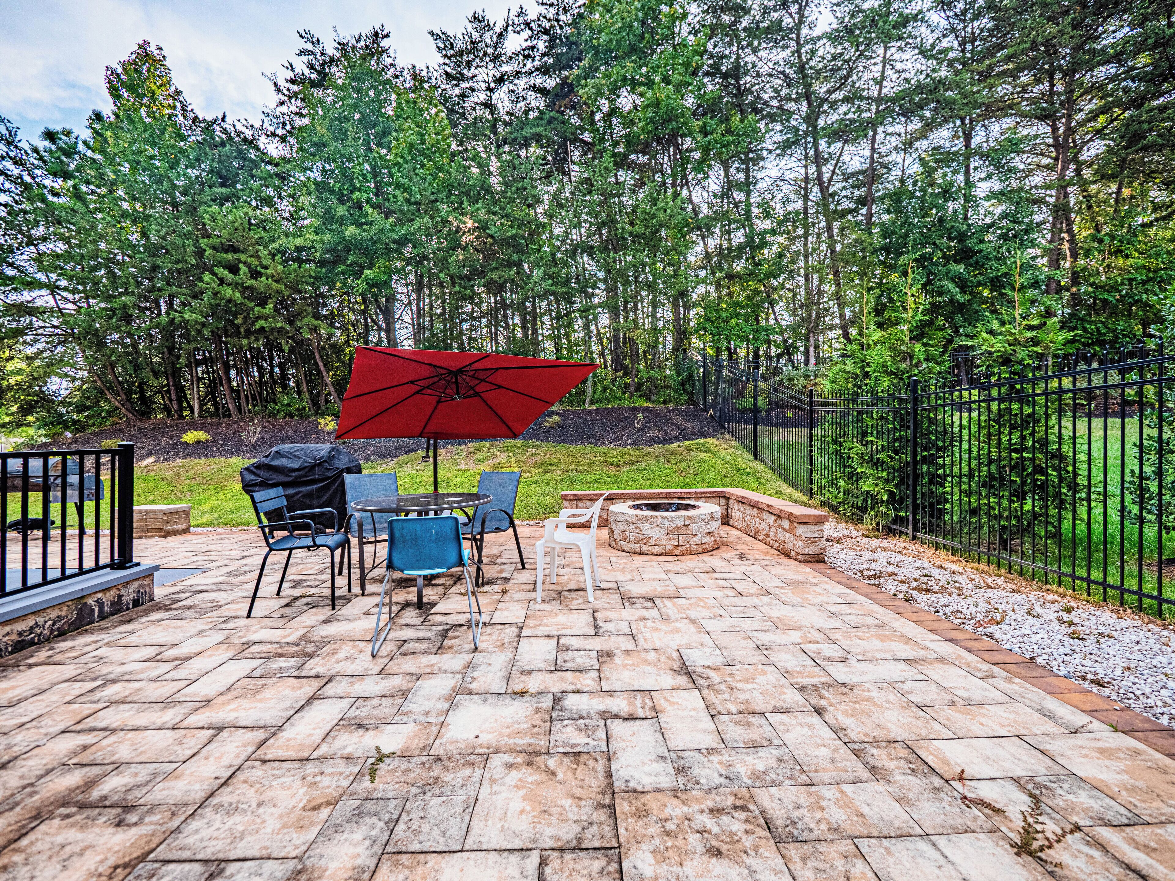 A patio with stone flooring, a round table, blue chairs, and a red umbrella.