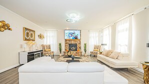 A modern living room with a white sectional sofa, a stone fireplace, and a flat-screen TV mounted above it.