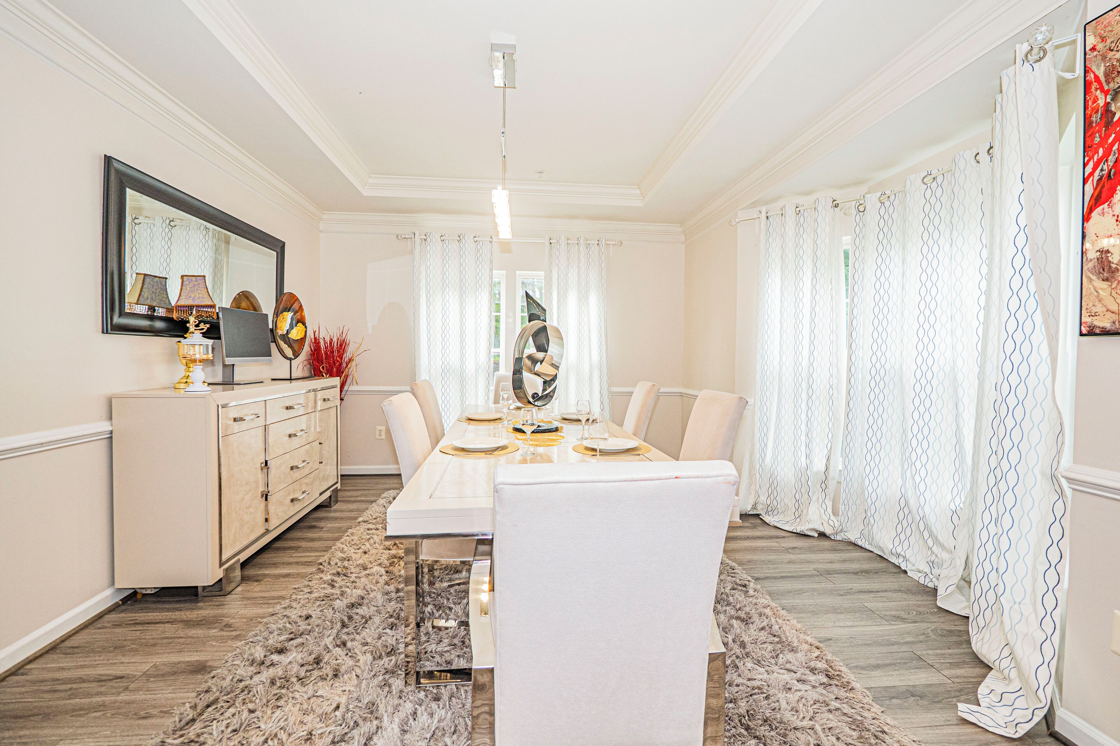 Comedor con una mesa blanca dispuesta para cuatro personas, un muro espejado y un espejo decorativo en la pared.