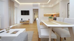 Un salon moderne avec un canapé blanc, une table basse et un coin repas comprenant une table blanche et des bancs.