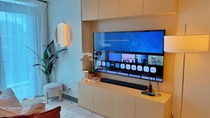 Un salon moderne avec un téléviseur à écran plat fixé à un mur en bois, une petite table d’appoint agrémentée d’un objet décoratif, une plante en pot et un coin salon confortable avec un coussin et un livre.