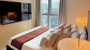 Une chambre d’hôtel moderne dotée d’un grand lit, d’un téléviseur à écran plat fixé au mur, d’une fenêtre avec des rideaux et d’une lampe de chevet.