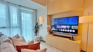 Un salon moderne avec un téléviseur à écran plat fixé à un mur en bois, un canapé avec des coussins, une petite table blanche et une plante en pot.