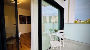 A balcony with a glass table and chairs, a potted plant, and a view of buildings. - Feel at Home in Bucharest (Bucharest)