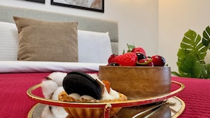A dessert tray with a cake and berries, a bed with white linens, a grey headboard, and a green plant. - Feel at Home in Bucharest (Bucharest)