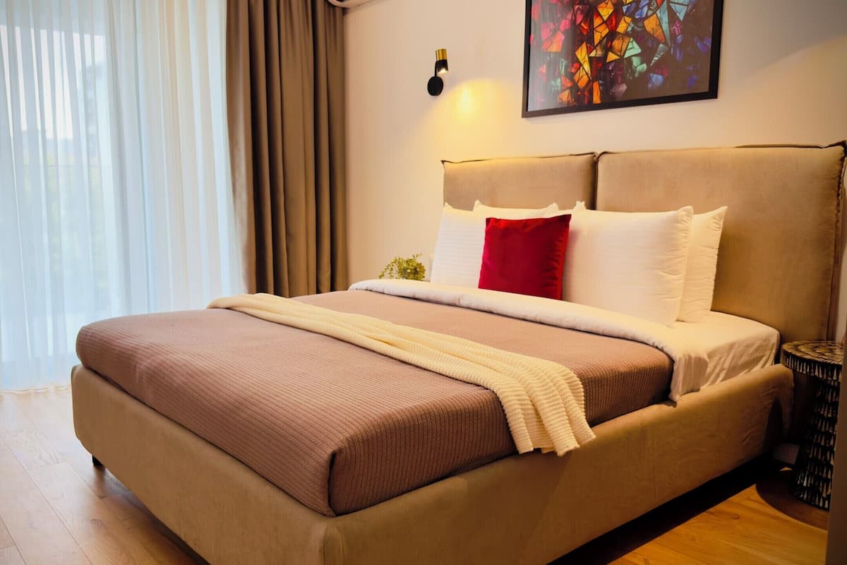 A hotel room with a large bed, a bedside table, a potted plant, and a painting on the wall.