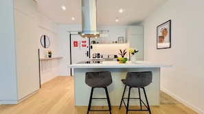 A modern kitchen with a central island, two bar stools, and a hanging light fixture. - Feel at Home in Bucharest (Bucharest)