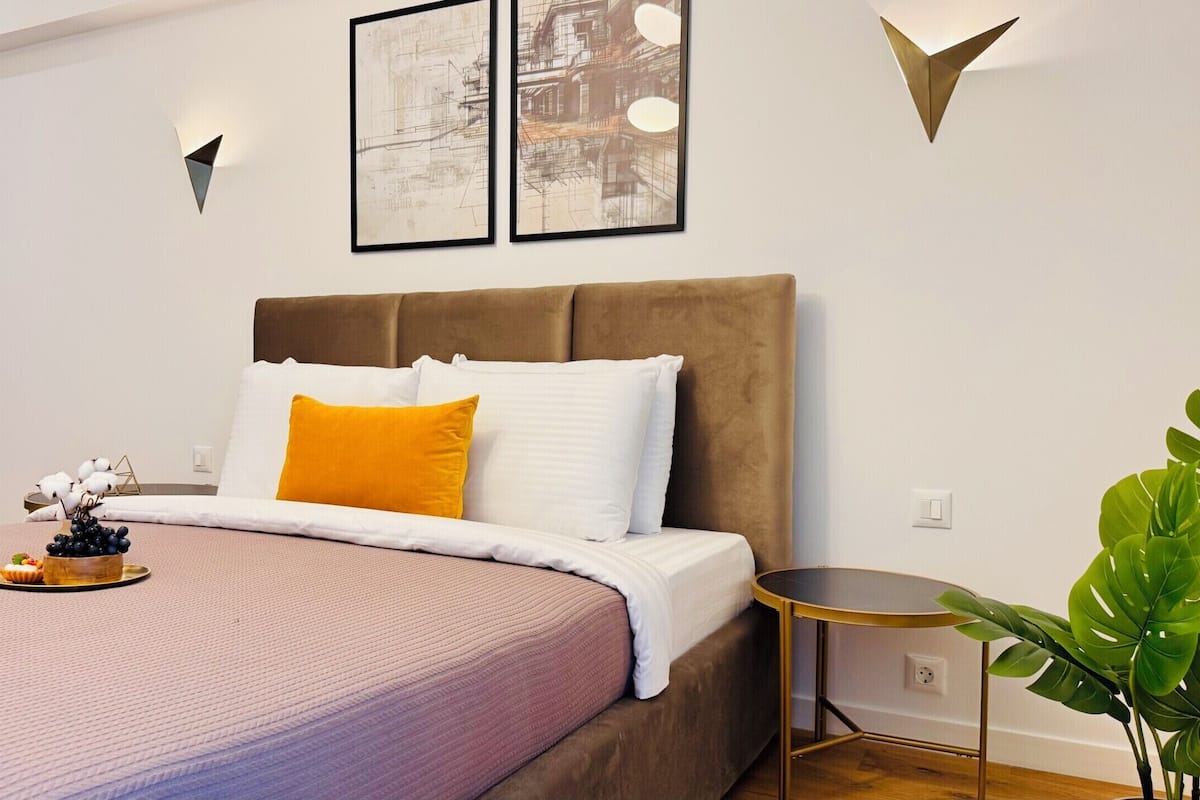 A modern bedroom with a bed, a bedside table, a wall-mounted light, and a framed picture.