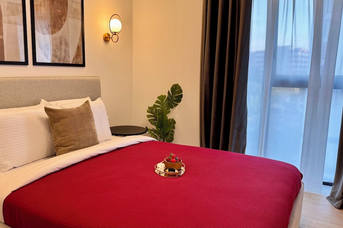 A hotel room with a bed, a nightstand, a potted plant, and artwork on the wall.