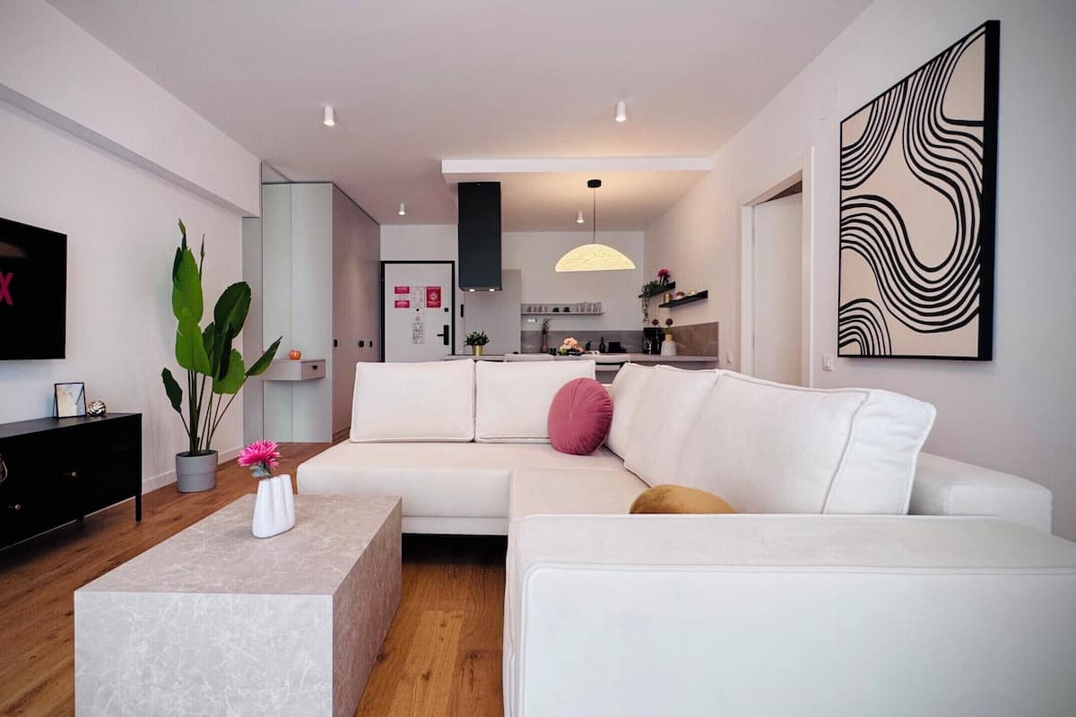 A modern living room with a white sofa, a coffee table, a TV, and a kitchen in the background.