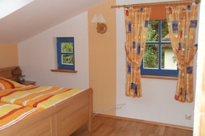 Une chambre à coucher avec un lit, une fenêtre avec des rideaux, une lampe fixée au mur et un petit cadre photo.