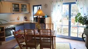 A kitchen with wooden cabinets, a dining table with chairs, a hanging lamp, and a view through a glass door. - Family-Friendly Holiday Home 'Märchengarten Fischer Un Sin Fru' (Putbus)