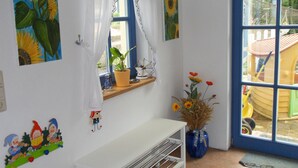 A room with a white wall, a window with a curtain, a white bench, a vase with flowers, and a door with a view of the outside. - Family-Friendly Holiday Home 'Märchengarten Fischer Un Sin Fru' (Putbus)