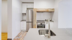 A compact kitchen with white cabinets, a stainless steel refrigerator, a built-in oven, and a sink with a modern faucet. - Nigrum Apartment, Santos, Lisbon (Lisboa)