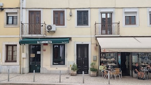 A building with a green awning labeled "LA CAMIONETTA" and a shop with glass display windows. - Nigrum Apartment, Santos, Lisbon (Lisboa)