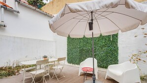 An outdoor patio with a table and chairs, a large umbrella, and a green wall. - Nigrum Apartment, Santos, Lisbon (Lisboa)