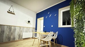 Zona pranzo con tavolo in legno e sedie bianche, parete decorata in blu e pianta pensile.