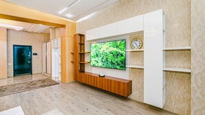 A modern living room with a flat-screen TV mounted on a wooden cabinet, a clock, and a door in the background. - Квартира супер отремонтирована. Комбинированная система. (Bakı)