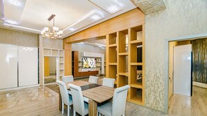 A modern dining area with a wooden table and white chairs, surrounded by built-in wooden shelves and a large flat-screen TV. - Квартира супер отремонтирована. Комбинированная система. (Bakı)