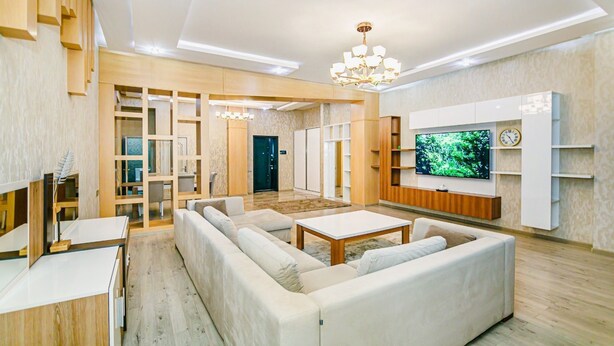 A modern living room with a large sectional sofa, a flat-screen TV, and built-in shelving. - Квартира супер отремонтирована. Комбинированная система. (Bakı)