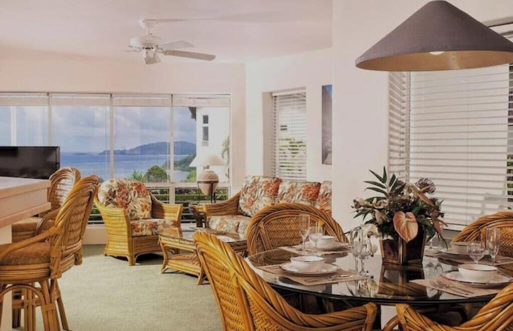 Un comedor con muebles de mimbre, una mesa de cristal y vistas al mar.
