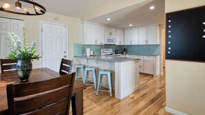 Una cocina moderna con armarios blancos, una isla central y un comedor con sillas de madera y un jarrón de flores.