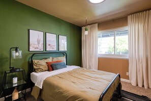 A bedroom with a bed, green walls, a window with curtains, and framed pictures on the wall.