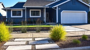 Una casa residencial con garaje, un porche delantero y un jardín bien cuidado con piedras de adoquín y plantas.