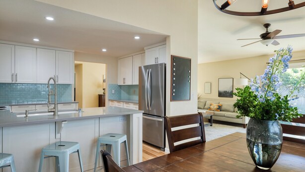 Una cocina moderna con armarios blancos, un refrigerador de acero inoxidable y un comedor con mesa de madera y taburetes de bar.