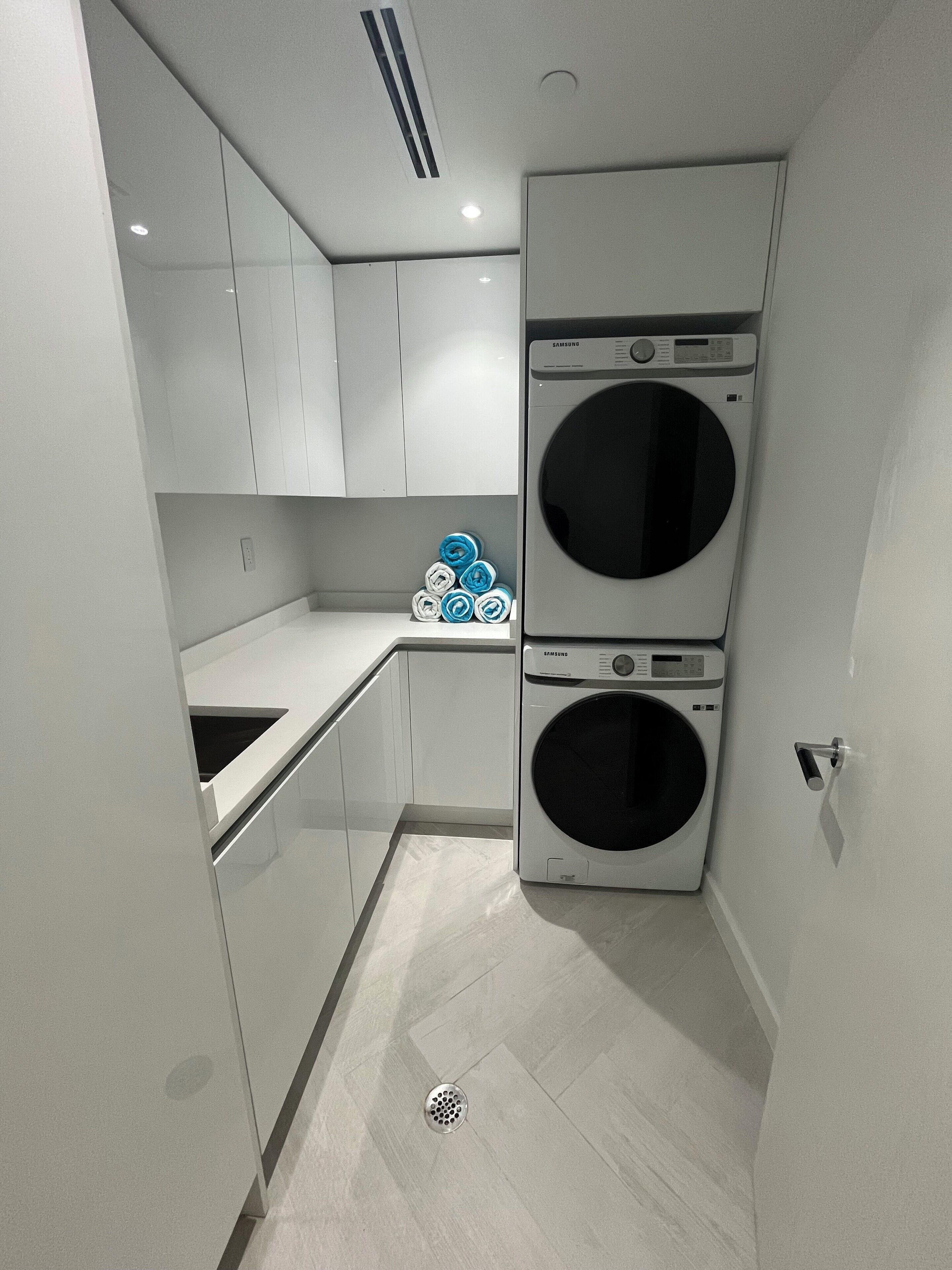 A compact laundry room with two stacked washing machines, a small countertop, and a cabinet.