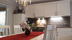 Een keuken met witte kastjes, een magnetron, een koffiezetapparaat en een vaas met bloemen op de tafel.