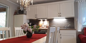 A kitchen with white cabinets, a microwave, a coffee maker, and a vase with flowers on the table.