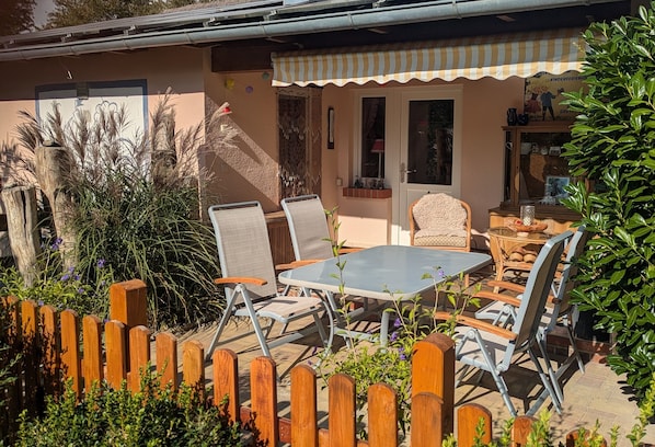 Une terrasse avec une table et des chaises, une clôture en bois et une maison dotée d’un auvent à rayures.